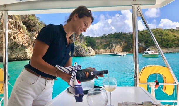 Pyratz Gourmet Sailing hostess serving a glass of white Burgundy wine to guests while the boat is anchored right in front of Little Bay. 