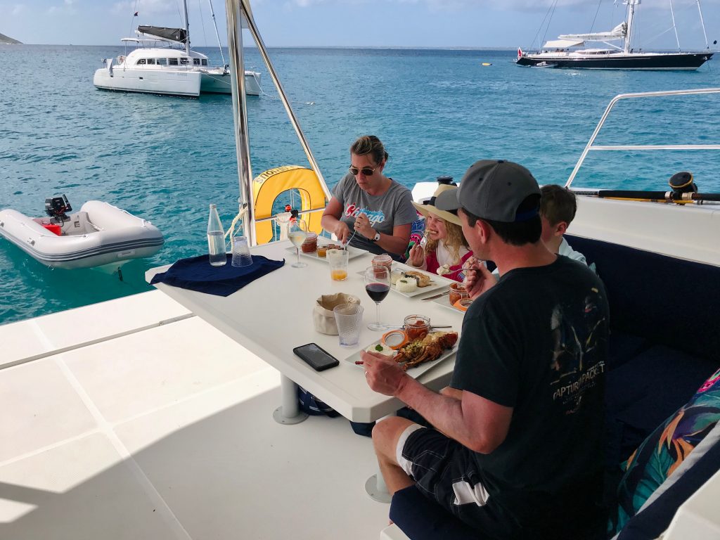 Parents and their two kids enjoying lobster, duck & fish for lunch on the turquoise water of Tintamarre. 