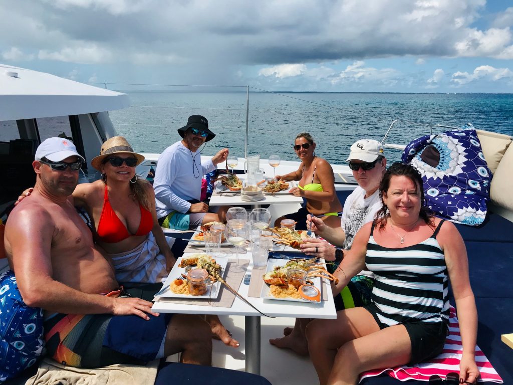 Gourp of friends having a gourmet lobster lunch on the bow deck of the catamaran, with plenty of rosé wine