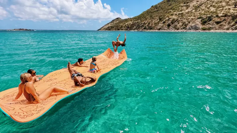 Group of people relaxing of a floating mat attached to a boat at Anse Marcel beach