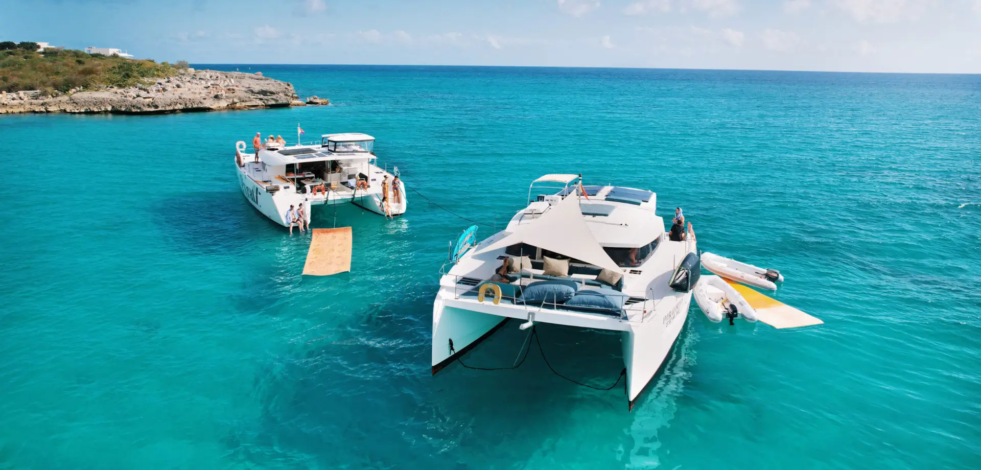 Luxury catamarans "Every Glorious" and "Galaxy" anchored at St Martin's coastline, seen from a drone. SUP boards and floating mats are in the water.