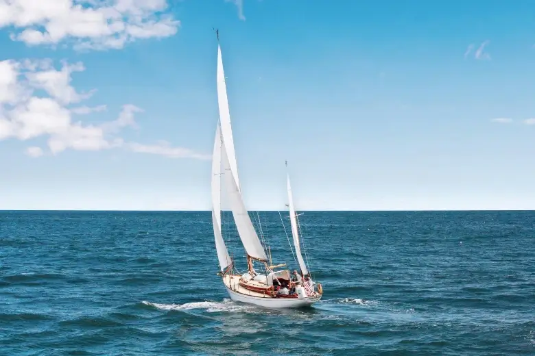 Drone picture of a sailboat in the ocean, as seen from behind