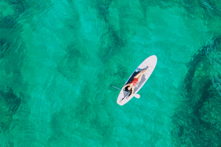 A girl lies on top of a SUP board as seen from a drone's-eye view