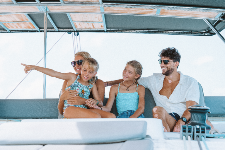 Family with two adults and their two daughters sitting on the deck of the boat during our sailing catamaran charter