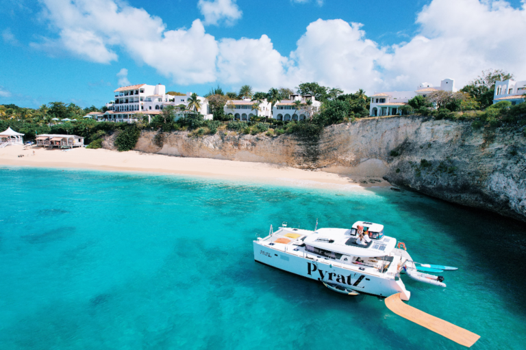 Motor catamaran from Pyratz anchored near a bay with cliffs in St Martin as seen from a drone