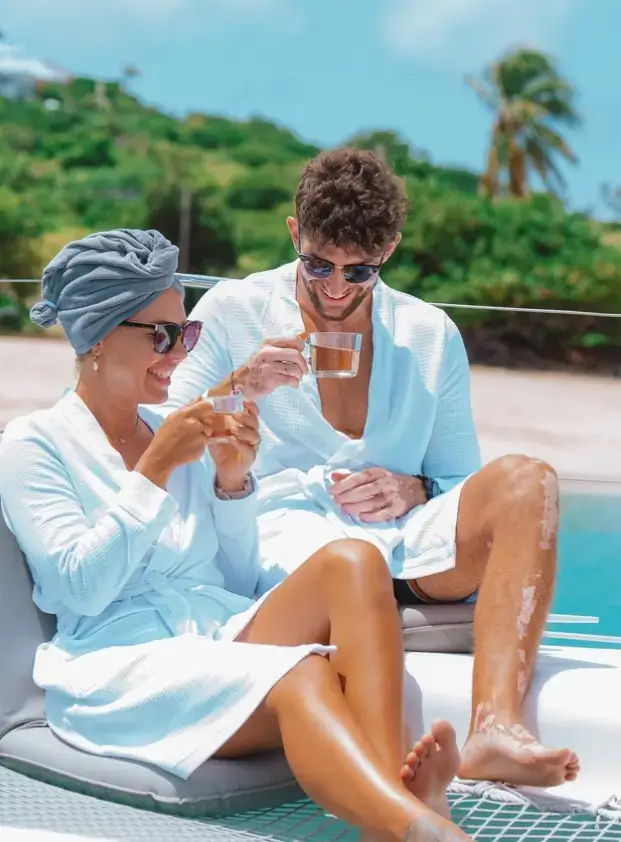 Couple in bathrobe having drinks on the deck of a catamaran during a sunny day in the Caribbean Sea
