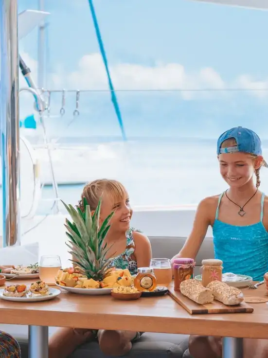 Kids having lunch onboard a sailboat in the Caribbean sea, with some fruits on the table